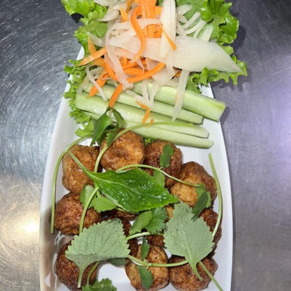 Vietnamese fried fish balls with fresh lettuce, shredded carrots, onions, and cucumber on a white plate.