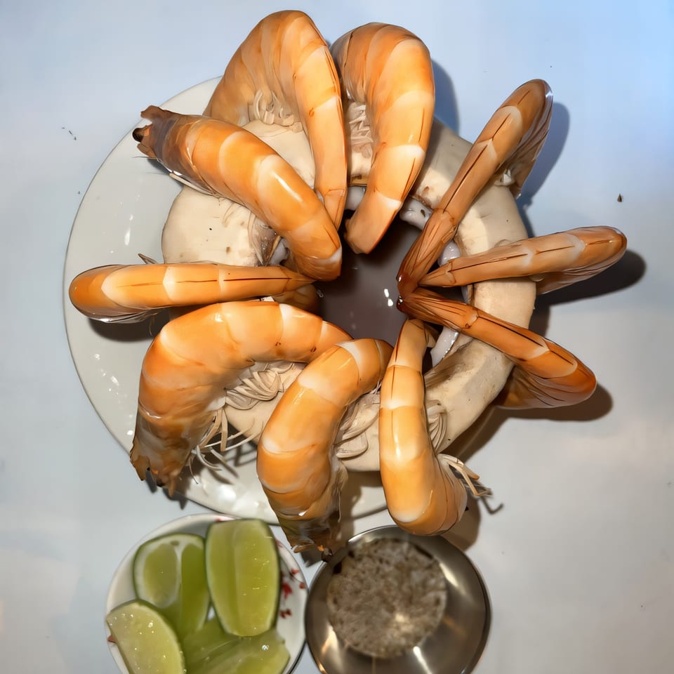 A plate of large, cooked shrimp arranged in a circle, with lime wedges and seasoning on the side.
