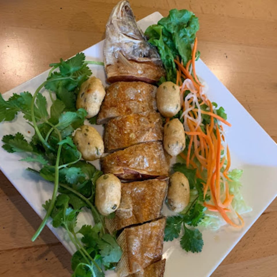 A whole fried fish, sliced, with small fried fish cakes, cilantro, lettuce, and shredded carrots.