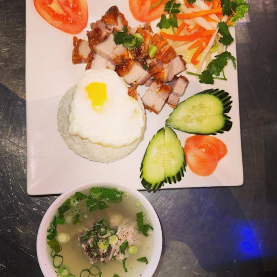 Vietnamese crispy pork belly with rice, a heart-shaped fried egg, pickled vegetables, and a side of soup.