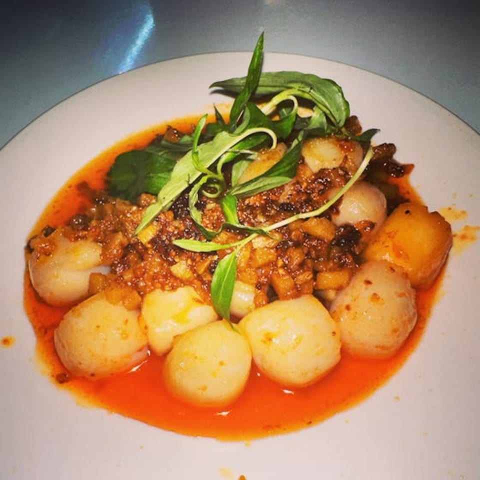 Vietnamese dish with round white and yellow pieces in a red sauce, topped with green herbs.