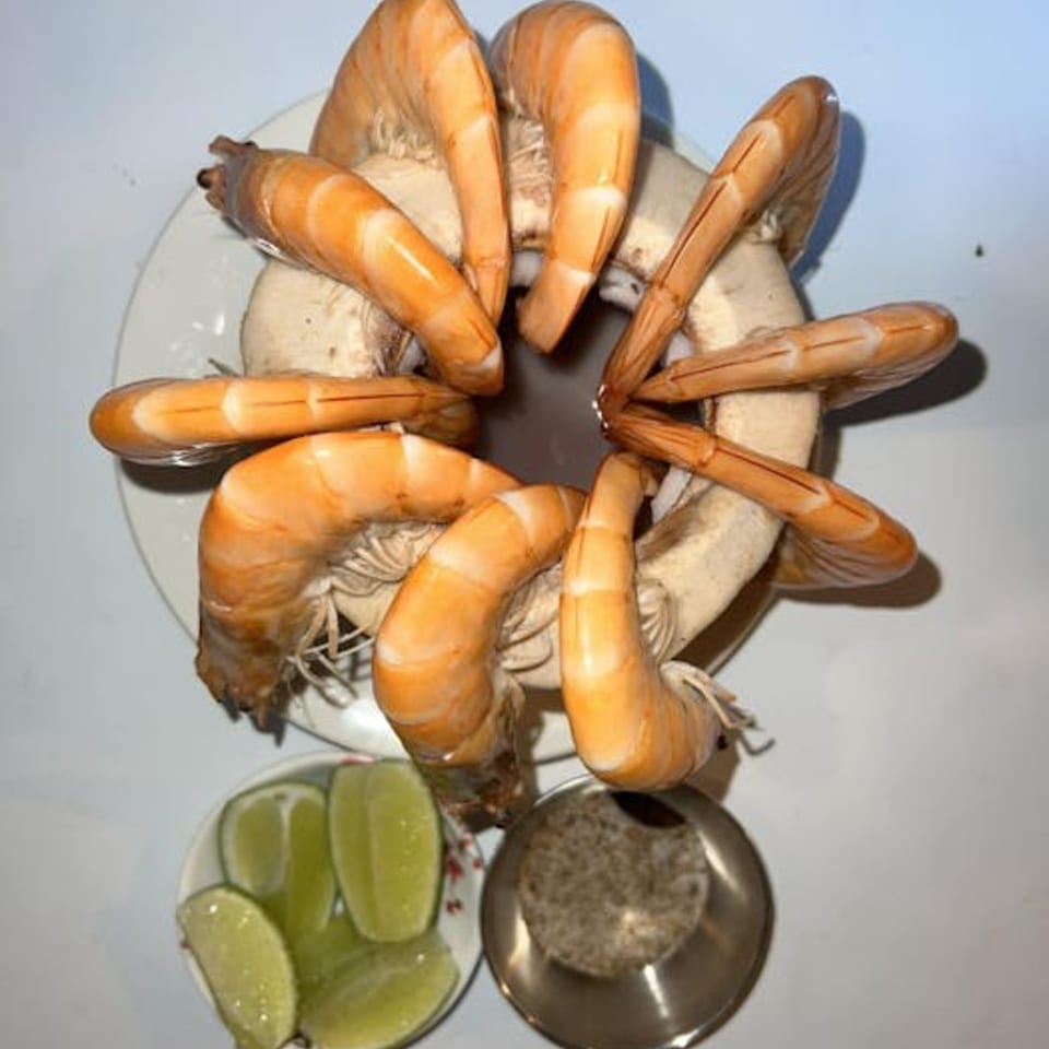 Boiled shrimp arranged in a circle with lime wedges and a small dish of spices.