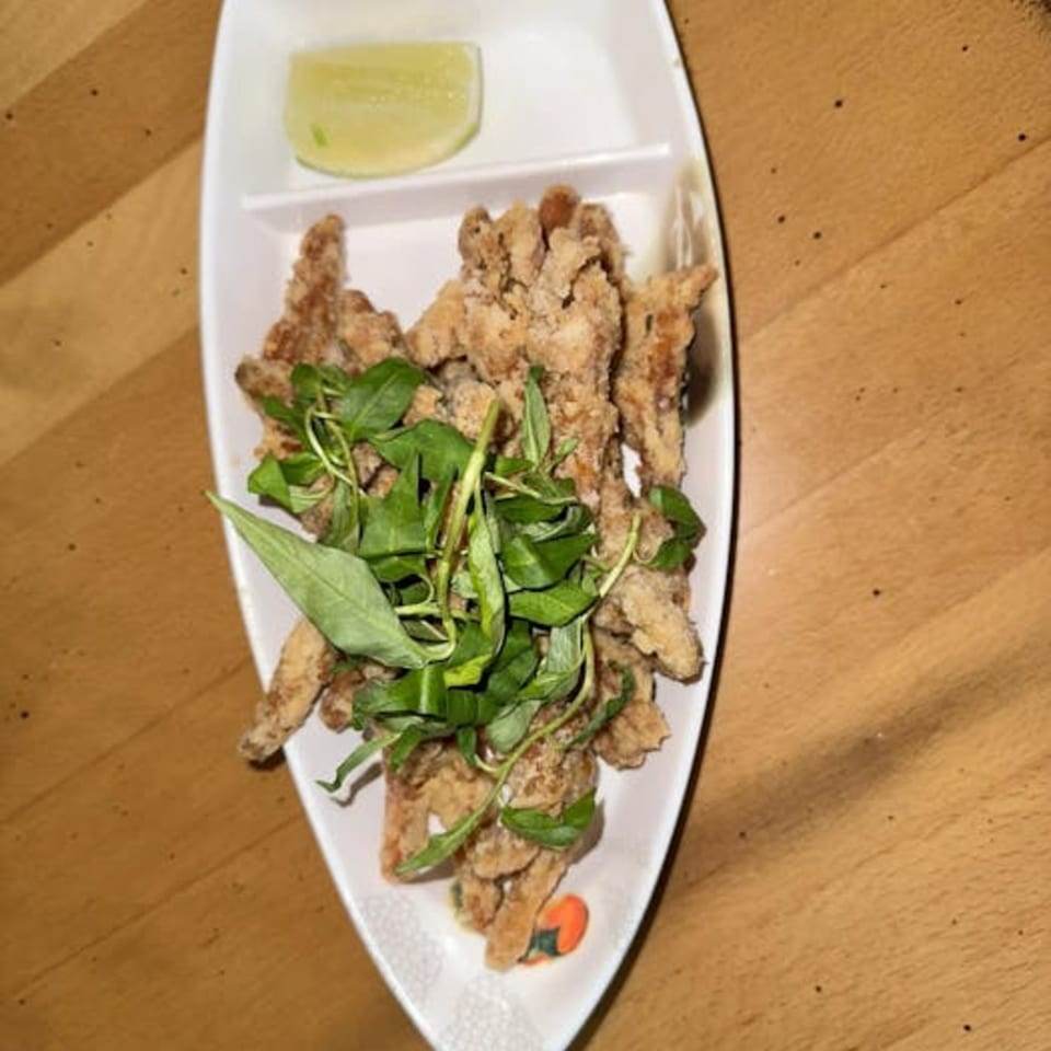 Crispy fried chicken pieces topped with fresh basil and a lime wedge on a white boat-shaped plate.