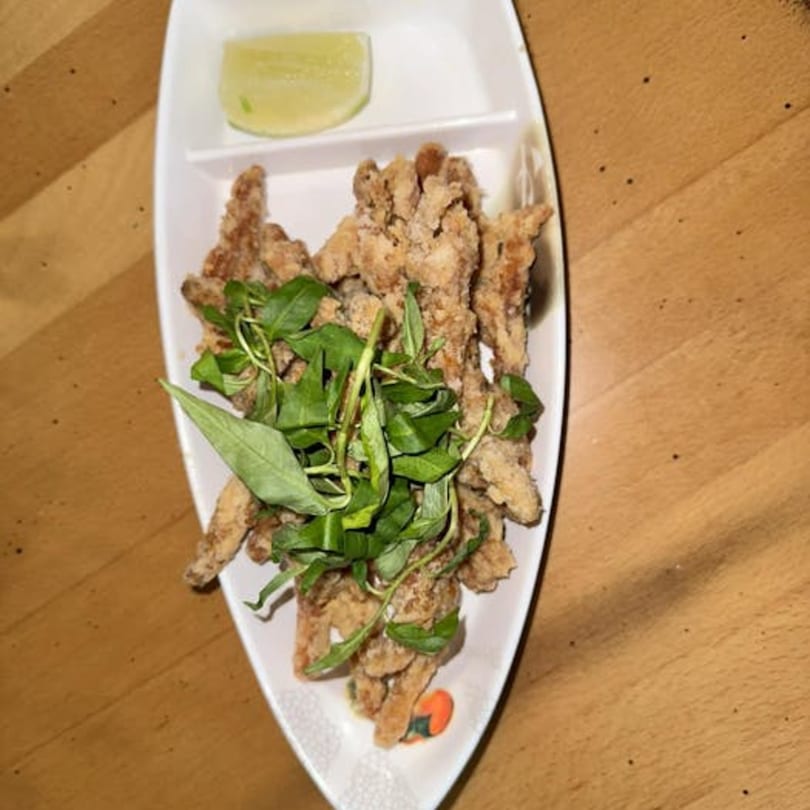 Crispy fried chicken pieces topped with fresh basil and a lime wedge on a white boat-shaped plate.