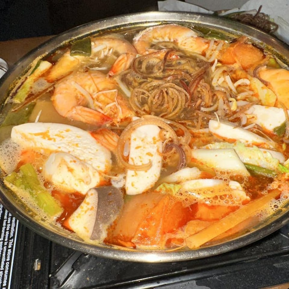 A large pot of Vietnamese hot pot, brimming with shrimp, noodles, vegetables, and tofu in a rich broth.