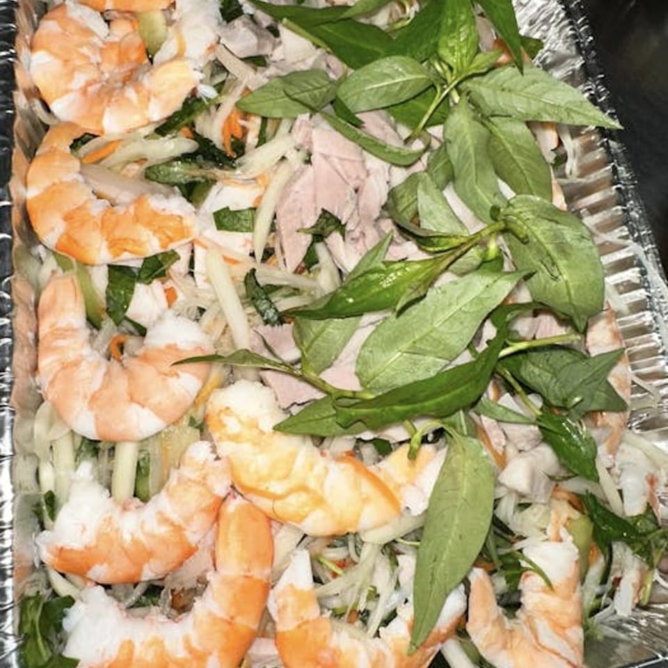 Vietnamese shrimp and chicken salad with herbs and vegetables in a foil container.