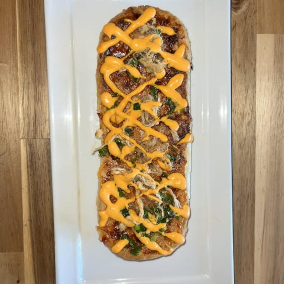 Vietnamese flatbread topped with shredded meat, green onions, and a yellow sauce drizzle on a white plate.