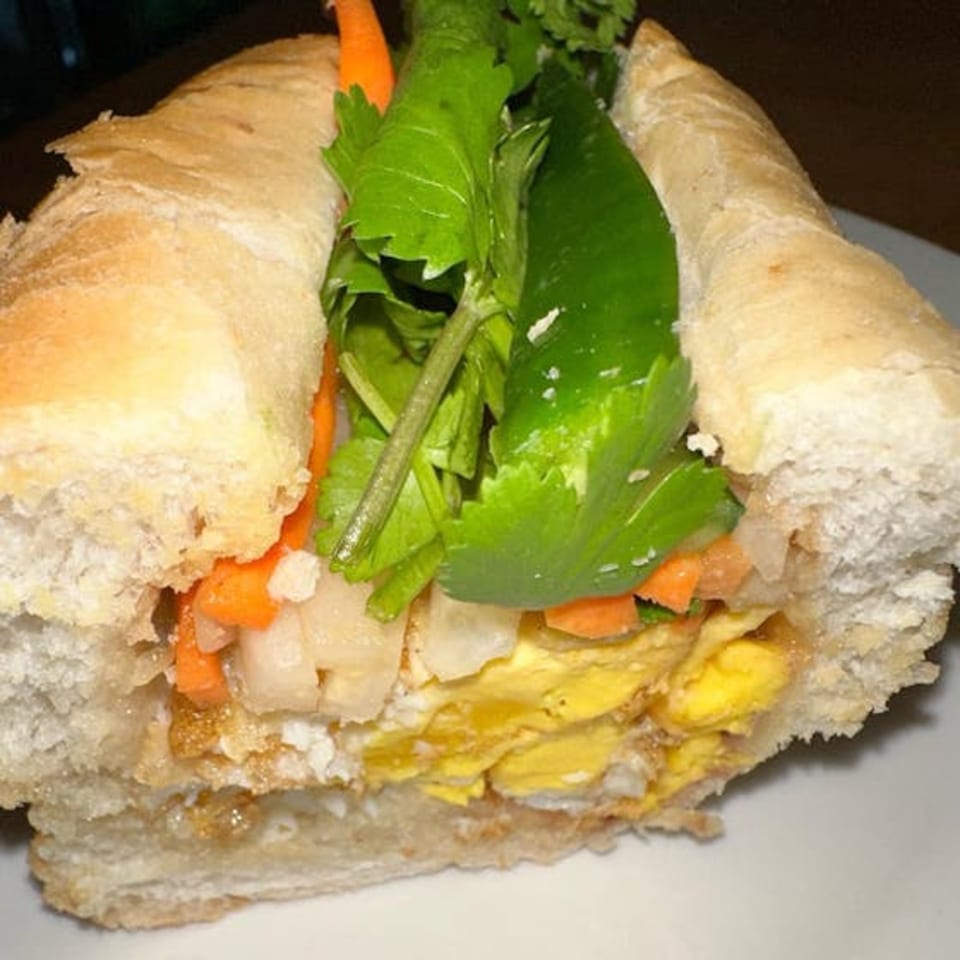 Close-up of a Vietnamese banh mi sandwich with egg, pickled vegetables, and cilantro.