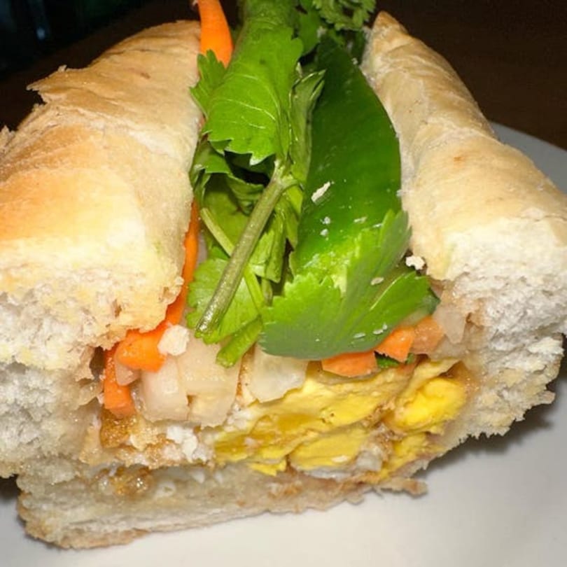 Close-up of a Vietnamese banh mi sandwich with egg, pickled vegetables, and cilantro.
