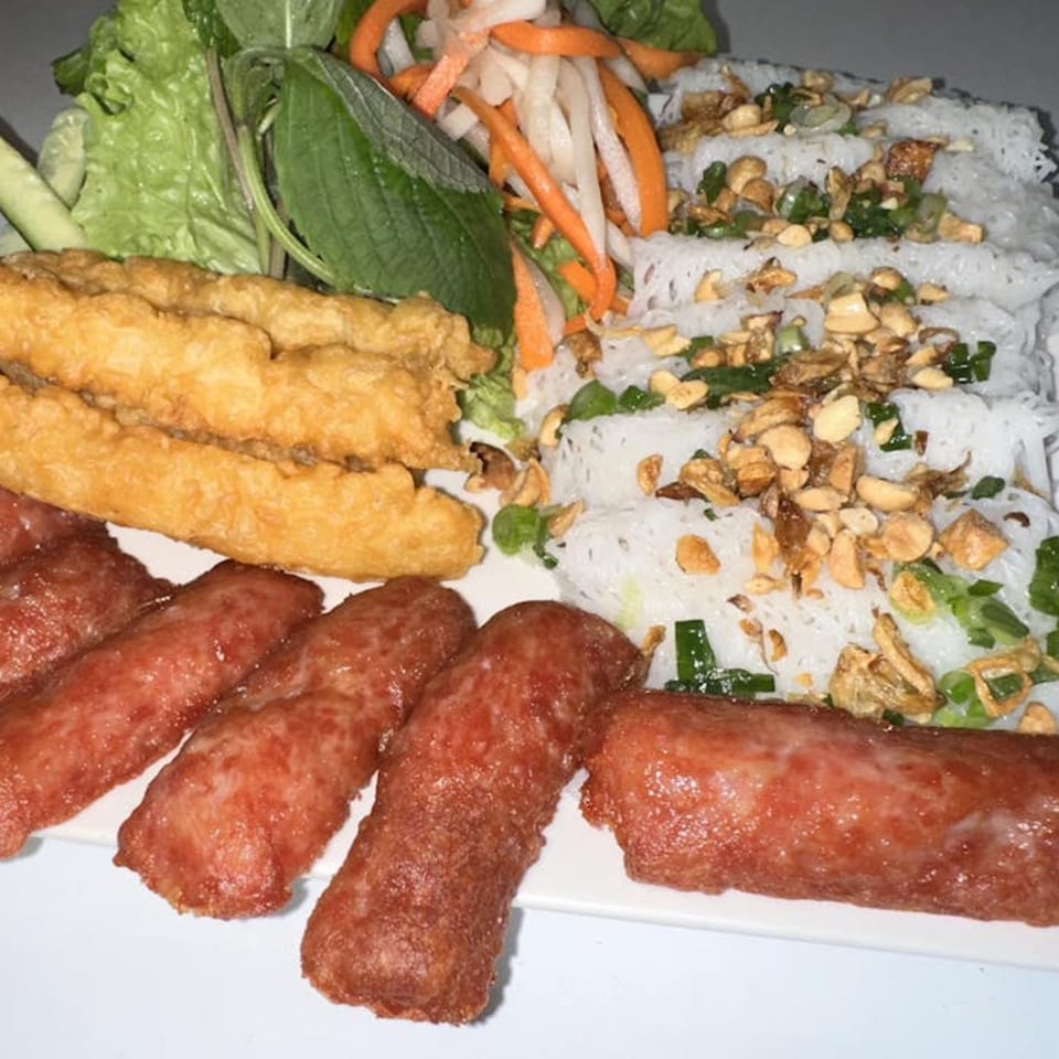 Vietnamese dish with fried spring rolls, red sausages, rice noodles, and fresh vegetables.