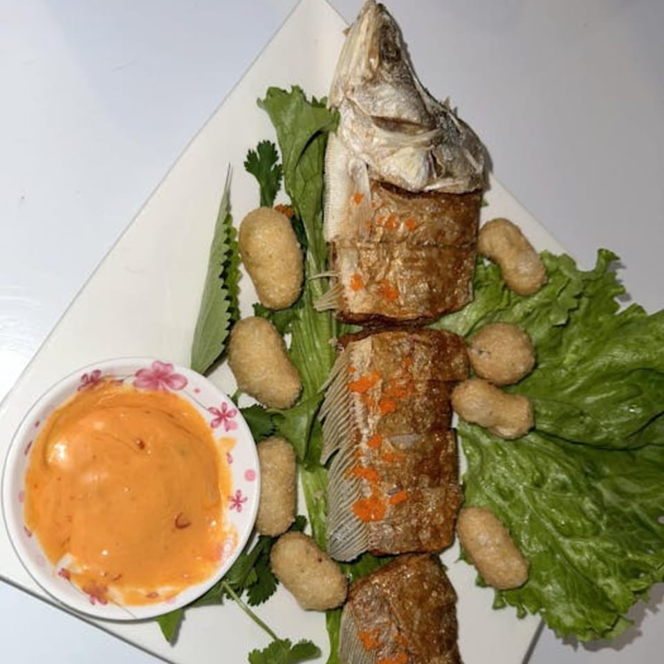 Fried fish with crispy skin, served with lettuce, small fried pieces, and a side of orange sauce.