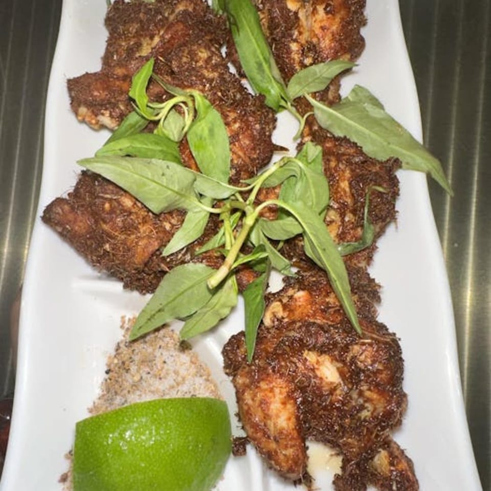 Crispy fried chicken pieces with green herbs, a lime wedge, and seasoning on a white plate.