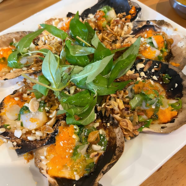 Vietnamese grilled scallops topped with herbs, peanuts, and orange roe on a white plate.
