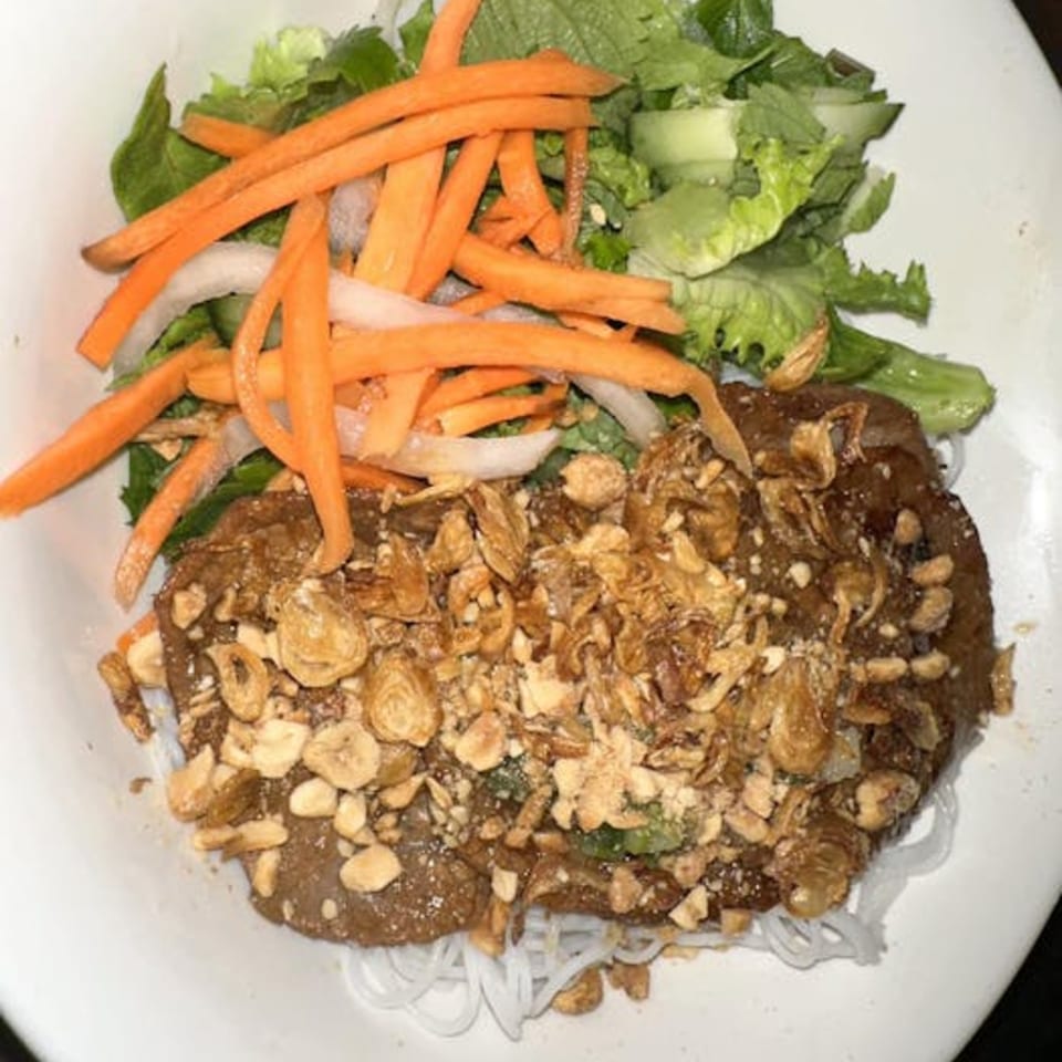 Vietnamese noodle dish with beef, fried garlic, peanuts, carrots, and lettuce in a white bowl.