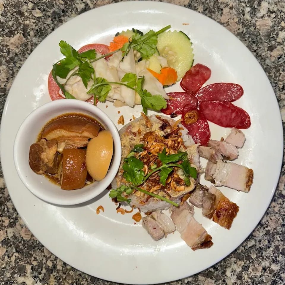 A Vietnamese platter with braised pork and egg, rice, sausage, crispy pork belly, and pickled vegetables.