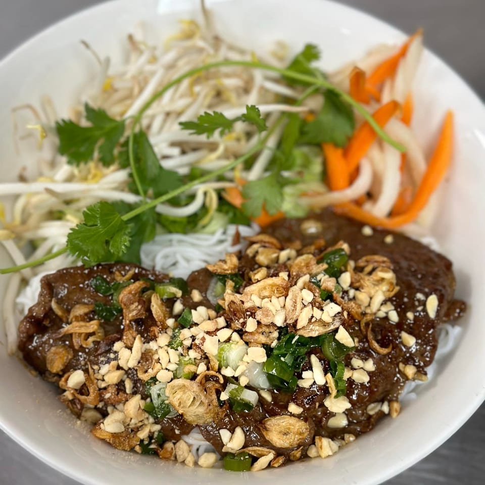 Vietnamese noodle bowl with dark meat, bean sprouts, pickled carrots, and peanuts in a white bowl.