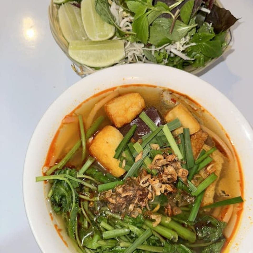 Vietnamese noodle soup with tofu, greens, and fried shallots, served with a side of fresh herbs and lime.