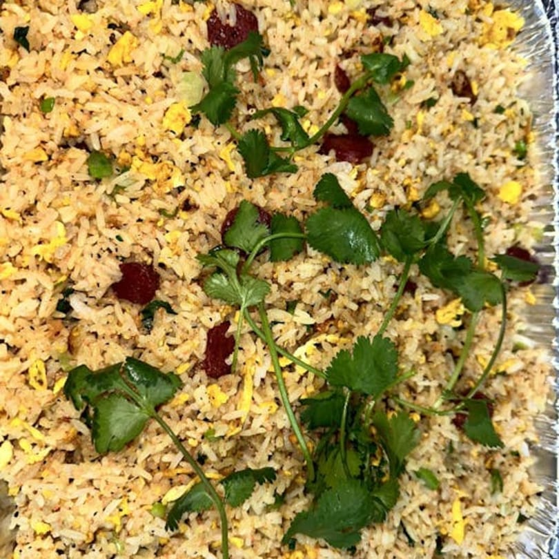 Vietnamese fried rice with scrambled egg, dark meat, and fresh cilantro in a foil container.