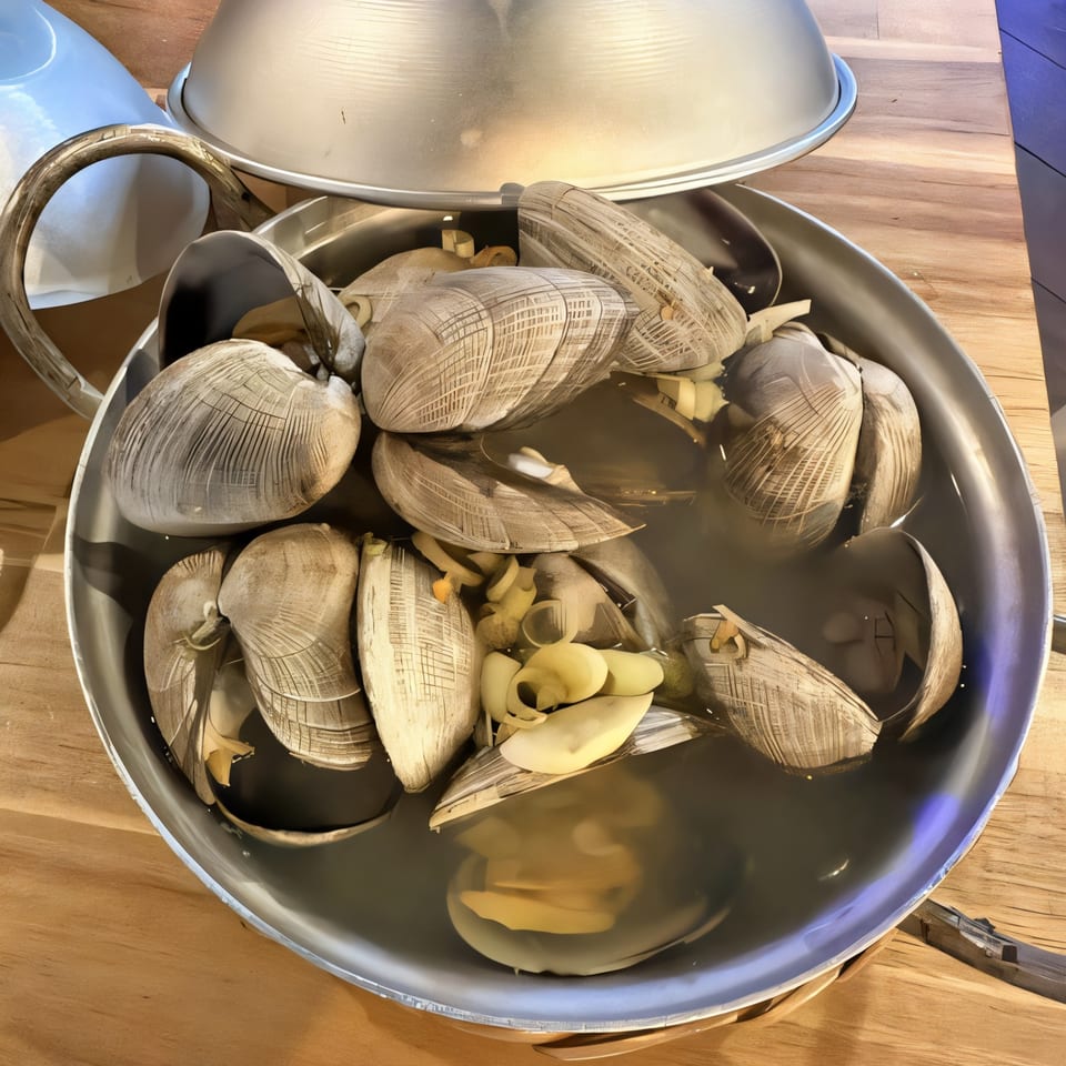Steamed clams with garlic in a metal pot, a Vietnamese dish from Quán Gì Quán Đêm Houston.