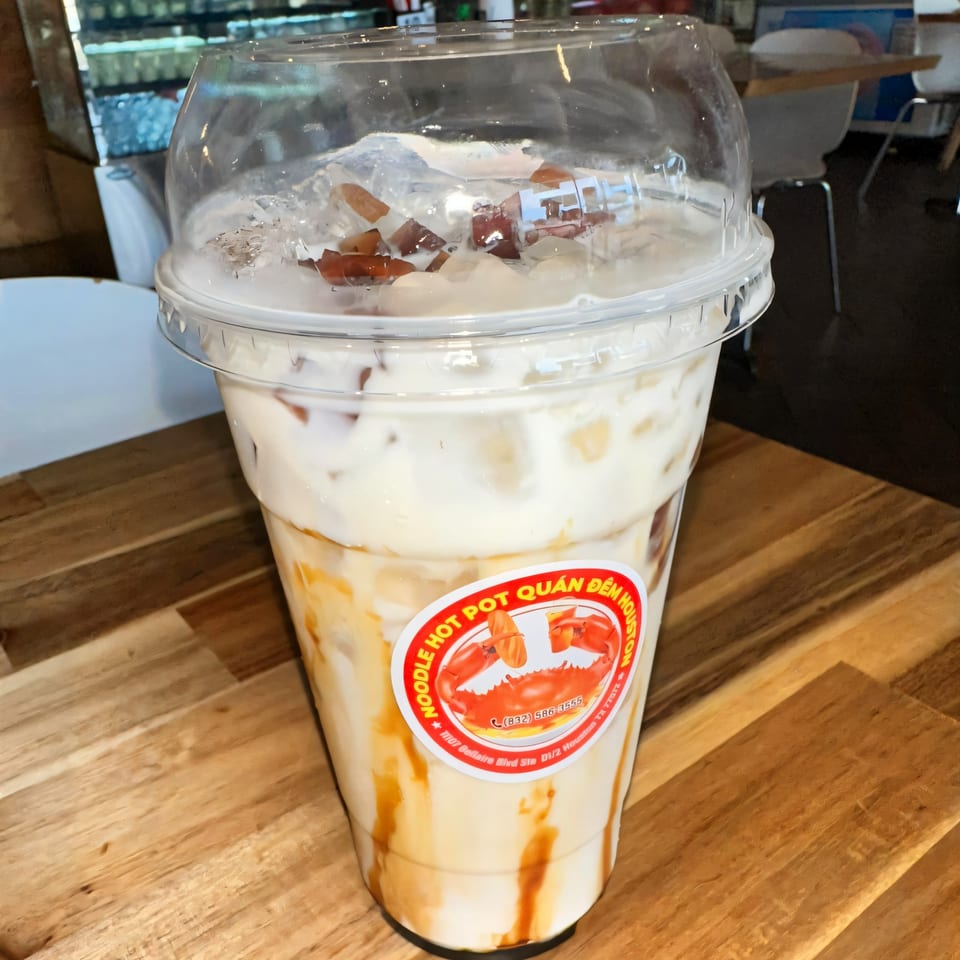 Iced Vietnamese milk tea with caramel swirls and toppings in a plastic cup on a wooden table.