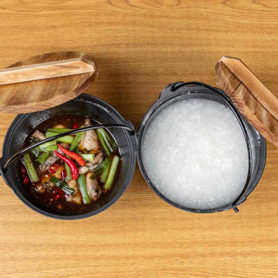 Two black pots on a wooden table, one with a savory dish and the other with white rice.