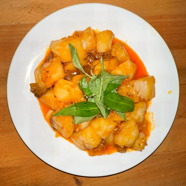 Vietnamese dish with white cubes in orange sauce, garnished with fresh green herbs on a white plate.
