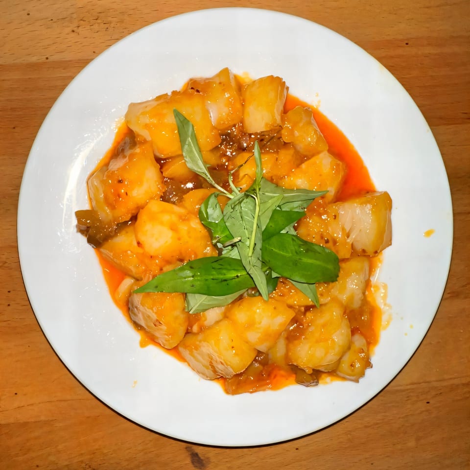 Vietnamese dish with white cubes in orange sauce, garnished with fresh green herbs on a white plate.
