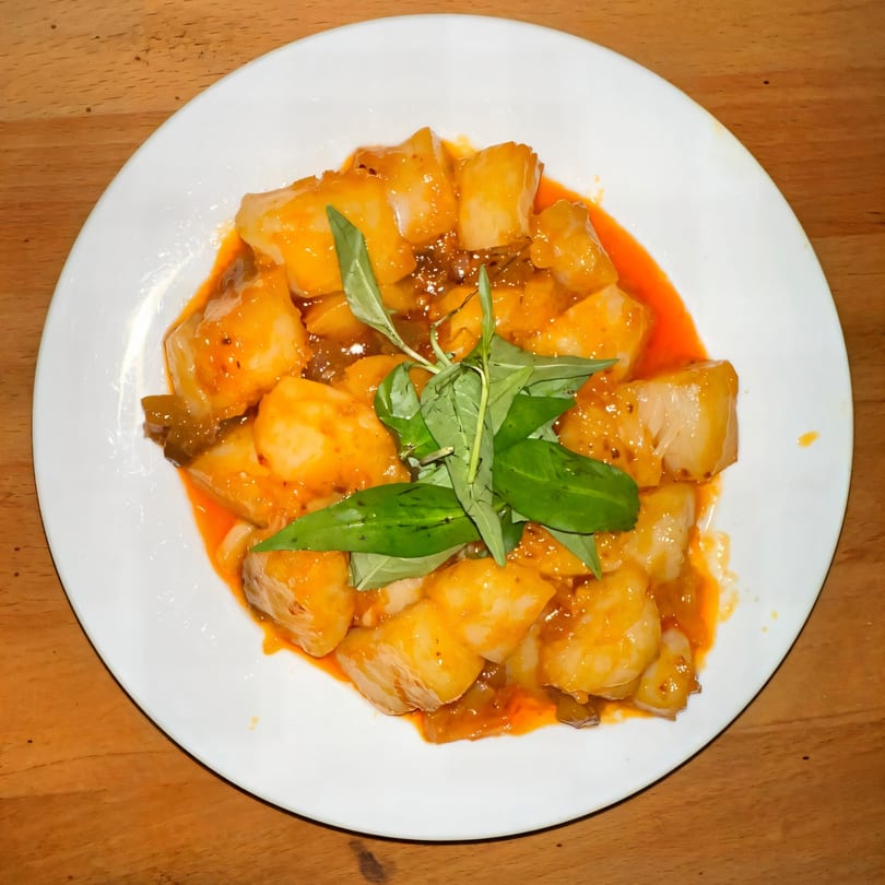 Vietnamese dish with white cubes in orange sauce, garnished with fresh green herbs on a white plate.
