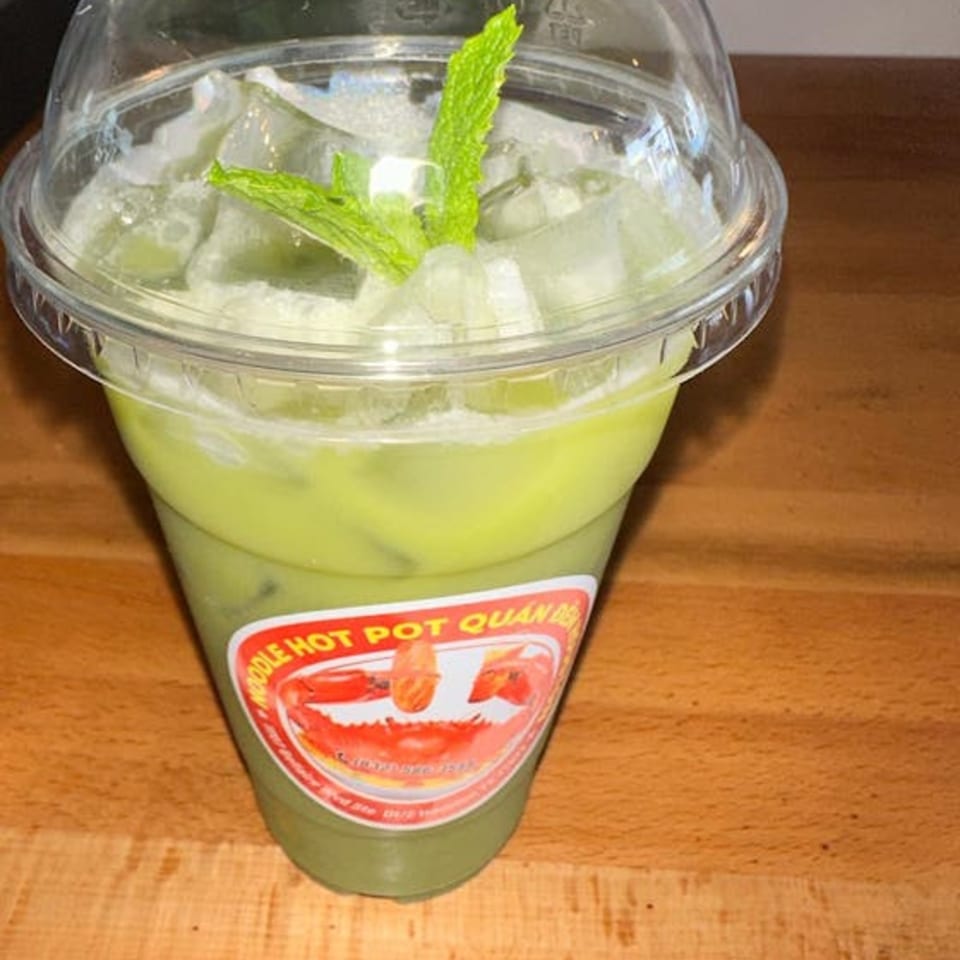 A green iced drink with mint leaves in a clear plastic cup with a red and white label.