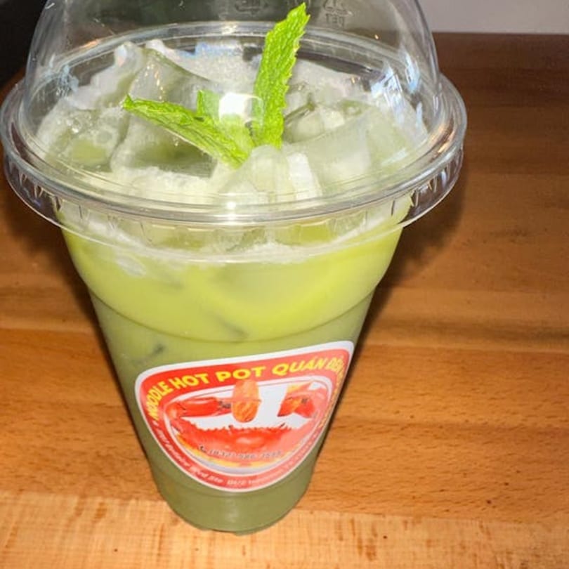 A green iced drink with mint leaves in a clear plastic cup with a red and white label.