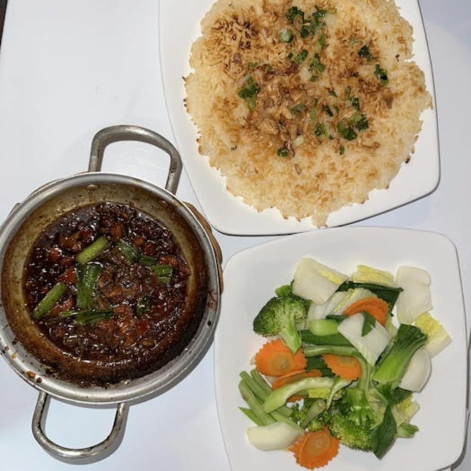 Vietnamese meal with crispy rice, braised pork in a hot pot, and a side of steamed vegetables.